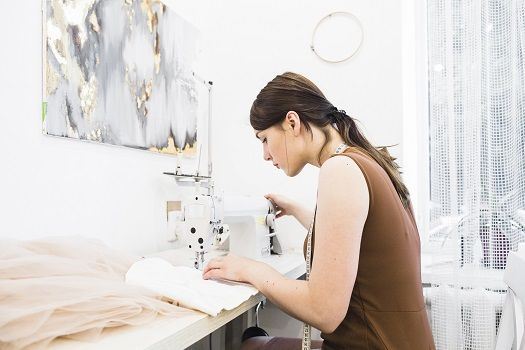 Blick auf junge Frau, die am Tisch sitzt und mit N&auml;hmaschine arbeitet.