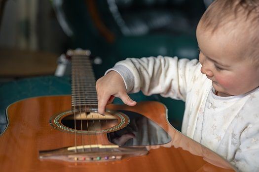 Das Baby erforscht mit Interesse eine Gitarre.