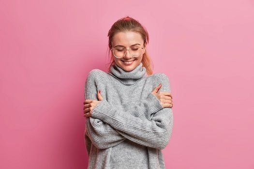 Glückliche junge Frau steht vor dem rosa Hintergrund und umarmt sich.