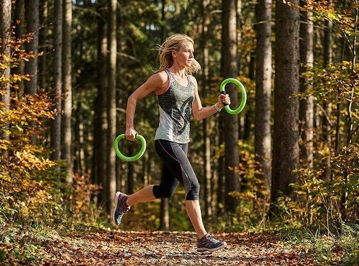 Sportliche Frau joggt im Wald mit smovey-Ringen in ihren Händen.