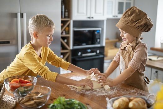 Zwei Kinder bereiten einen Teig in der K&uuml;che zu.