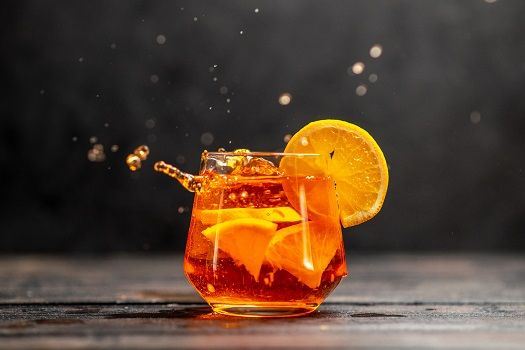 Blick auf Glas mit Cocktail und Orangen-Stückchen.